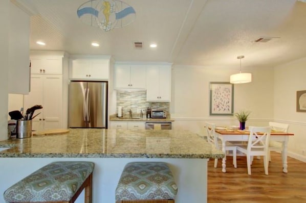 A modern kitchen with white cabinetry, a stainless steel refrigerator, and a granite countertop.