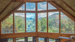 Una habitación con amplios ventanales que ofrecen vistas a un valle boscoso.
