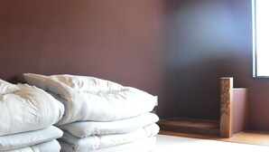 Una habitación con una pila de almohadas contra la pared, un banco de madera y una ventana con luz natural.