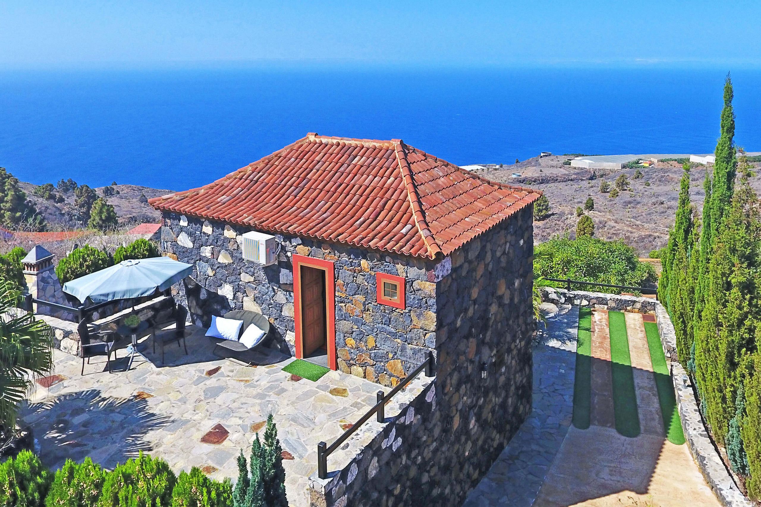 Une maison en pierre avec un toit recouvert de tuiles rouges, une terrasse avec des meubles d’extérieur et une vue sur la mer.