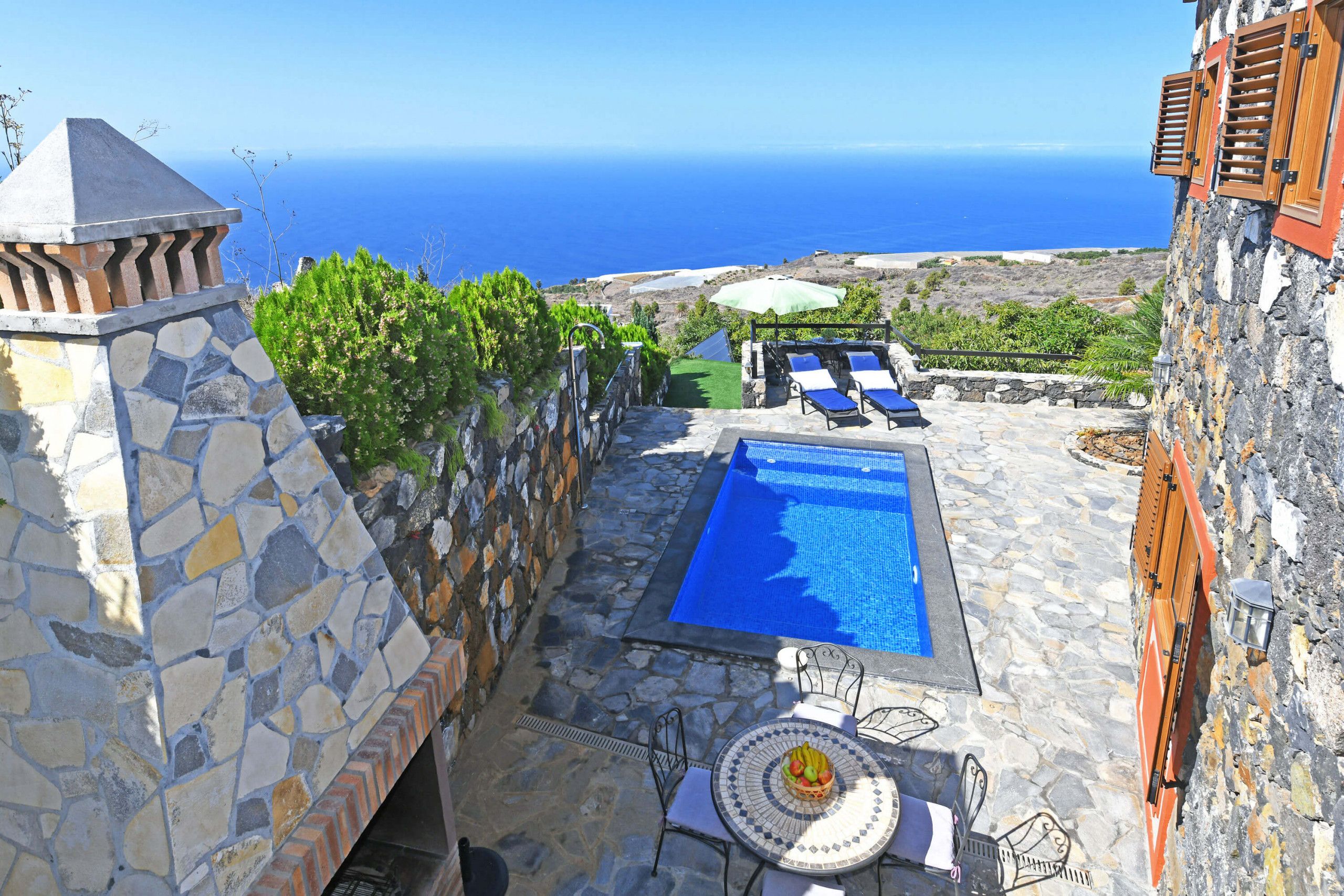 Un edificio de piedra con piscina, sillas de descanso y vista al mar.