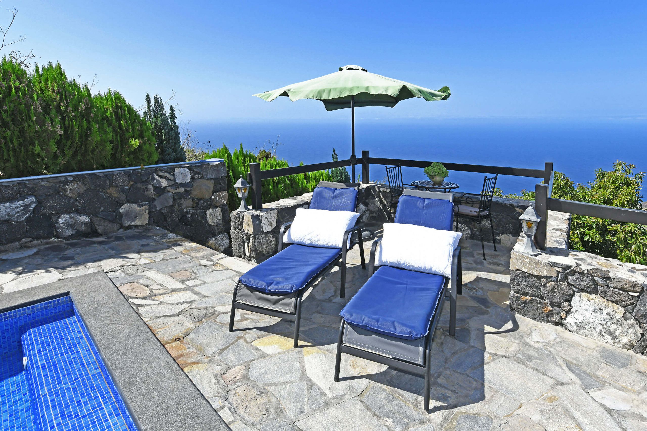 Une terrasse en pierre avec deux chaises longues et une table, donnant sur une étendue d’eau.