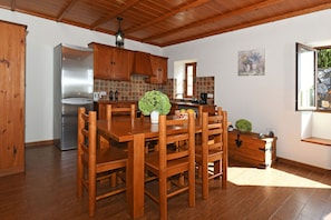 A kitchen with wooden cabinets, a stainless steel refrigerator, a dining table with chairs, and a small potted plant.