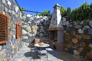A stone patio with a round table and chairs, a stone wall, and a chimney.