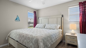 Een slaapkamer met een bed, een nachtkastje met een lamp, een raam met jaloezieën en een decoratie aan de muur.