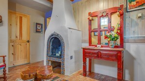 Un interior rústico con una puerta de madera, una chimenea decorativa, un aparador de madera rojo y una alfombra estampada.
