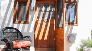 Una puerta de madera con un panel de vidrio, una silla de mimbre con un cojín rojo y una pequeña ventana con marco de madera.