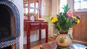 Una mesa de madera con un florero, un espejo y un papel tapiz estampado.