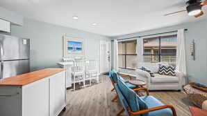 Une cuisine moderne dotée d’un réfrigérateur encastré, d’un coin repas avec des chaises blanches et d’une grande fenêtre donnant sur le balcon.