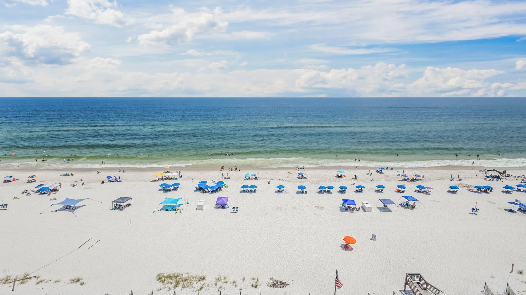 A beach with numerous umbrellas and sun loungers, a sandy shore, and the ocean in the background.