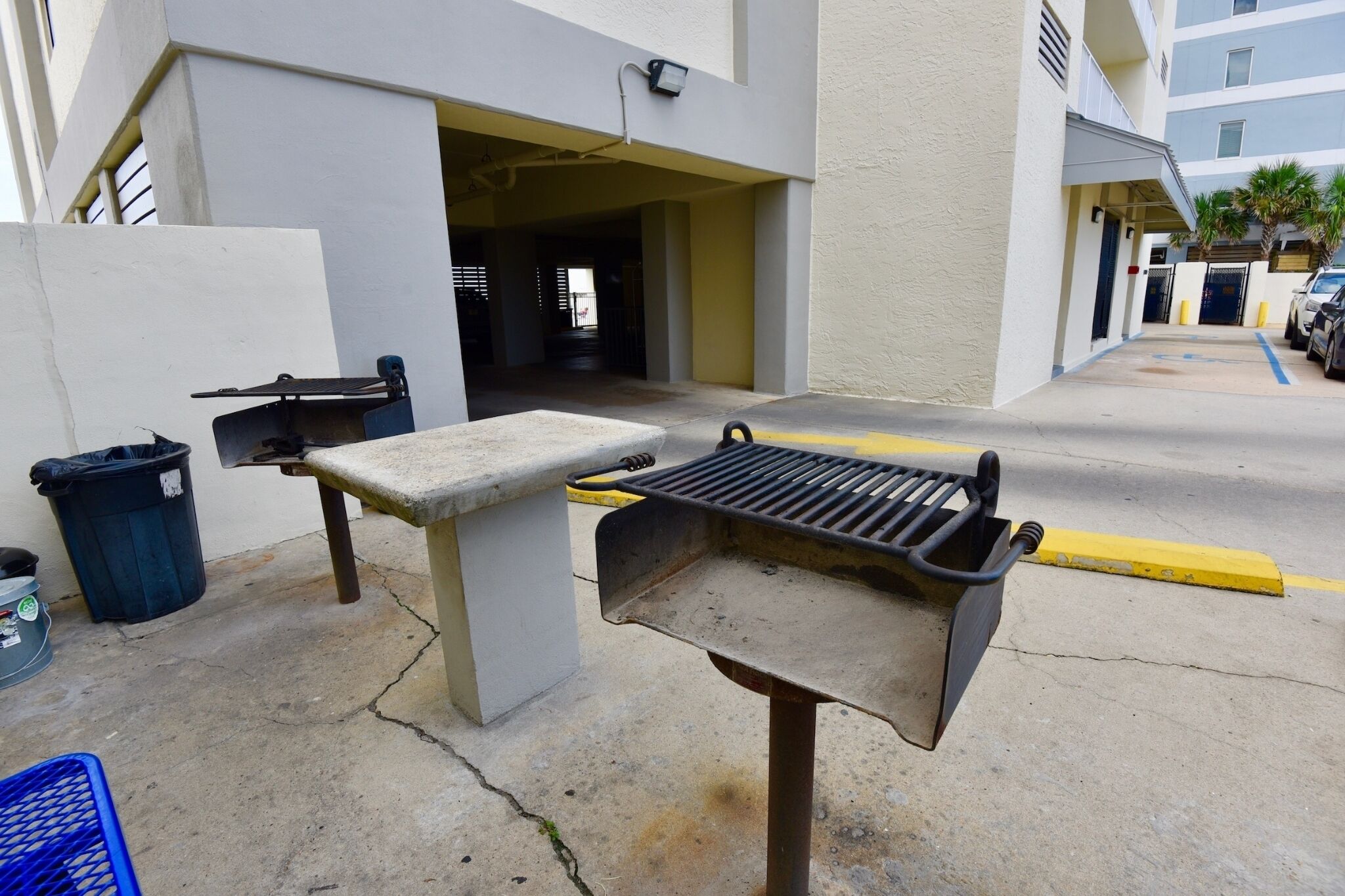 Una parrilla para barbacoa al aire libre y un contenedor de basura en un estacionamiento.