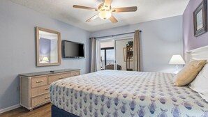 Ein Schlafzimmer mit einem Bett, einem Schminktisch, einem Fernseher und einem Deckenventilator.