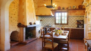 A rustic kitchen with a stone fireplace, wooden chairs, and a tiled backsplash. - Charming house Alou with a stunning pool, peaceful location and beautiful garden (Felanitx)