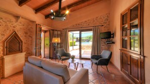 A cozy living room with a sofa, chairs, a TV, and a stone wall. - Charming house Alou with a stunning pool, peaceful location and beautiful garden (Felanitx)