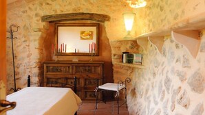 A rustic room with a stone wall, a wooden dresser, a chair, and a lit wall lamp. - Charming house Alou with a stunning pool, peaceful location and beautiful garden (Felanitx)