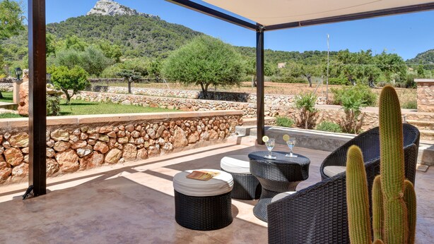 An outdoor patio with wicker furniture, a stone wall, and a view of a mountainous landscape. - Charming house Alou with a stunning pool, peaceful location and beautiful garden (Felanitx)
