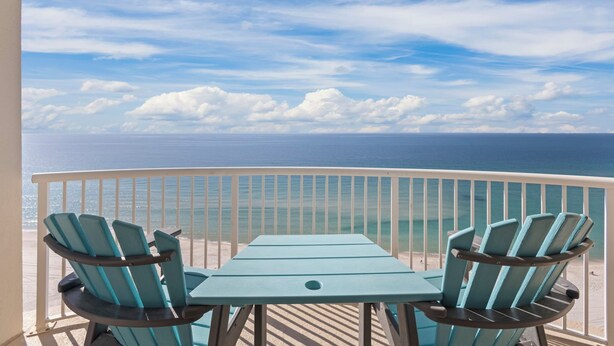 Un balcon avec deux fauteuils Adirondack et une table, donnant sur une plage et l’océan.