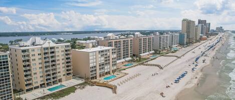 A beachfront hotel with multiple high-rise buildings, a sandy beach, and a pool area.
