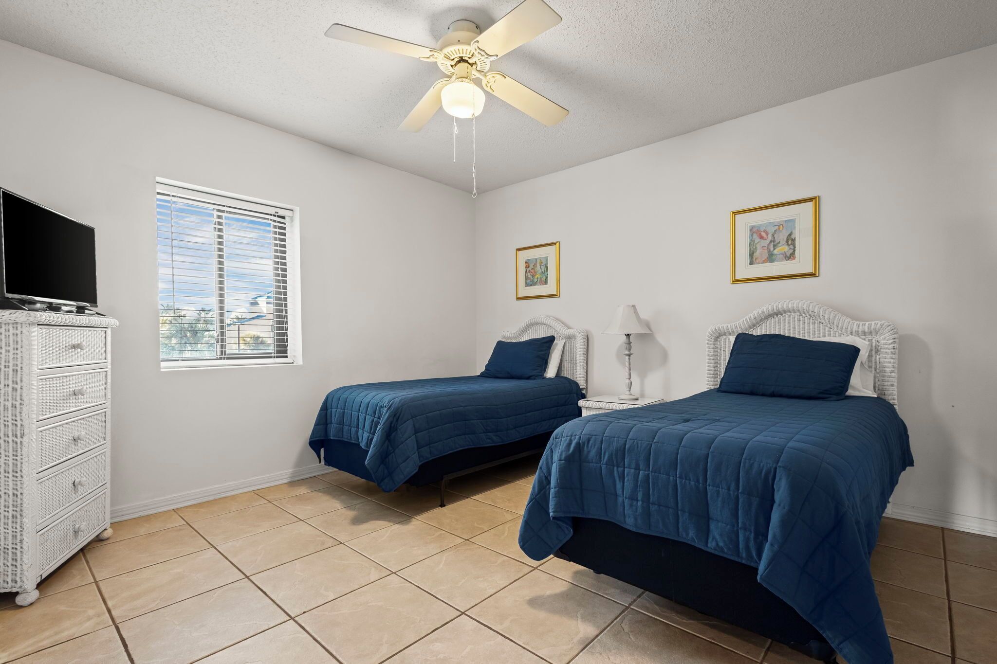 A bedroom with two beds, a ceiling fan, a TV, and a window with blinds.