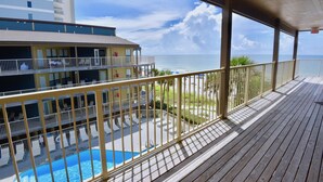 A wooden deck with a pool and lounge chairs, overlooking a beach and a building with multiple balconies. - Popular beachside condo for 6 (Gulf Shores)