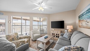 A living room with a ceiling fan, a flat-screen TV, a sofa, a chair, and a coffee table. - Popular beachside condo for 6 (Gulf Shores)