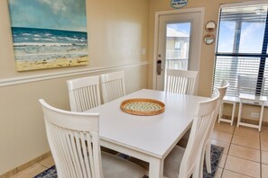 Enjoy meals in this dining area with a table, chairs, and a beautiful beach scene painting on the wall.