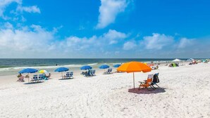 Een strand met rijen blauwe en oranje parasols, wit zand en de oceaan op de achtergrond.