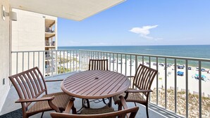 Een balkon met een ronde tafel en stoelen, met uitzicht op een strand met parasols en mensen.