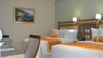 A hotel room with two beds, a desk, and a painting of a coastal scene.