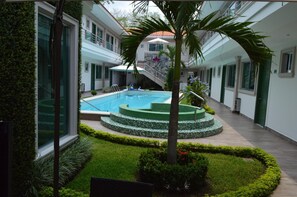 A modern hotel courtyard with a swimming pool, palm trees, and a staircase leading to an upper level.