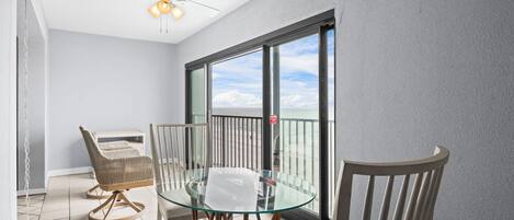 A balcony with a glass table and chairs, a ceiling fan, and a view of the ocean.