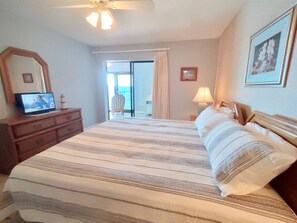 A hotel room with a bed, a TV on a dresser, a chair, and a balcony with a view. - Beachfront condo with glass-enclosed balcony ~ Basic furnishings (Gulf Shores)