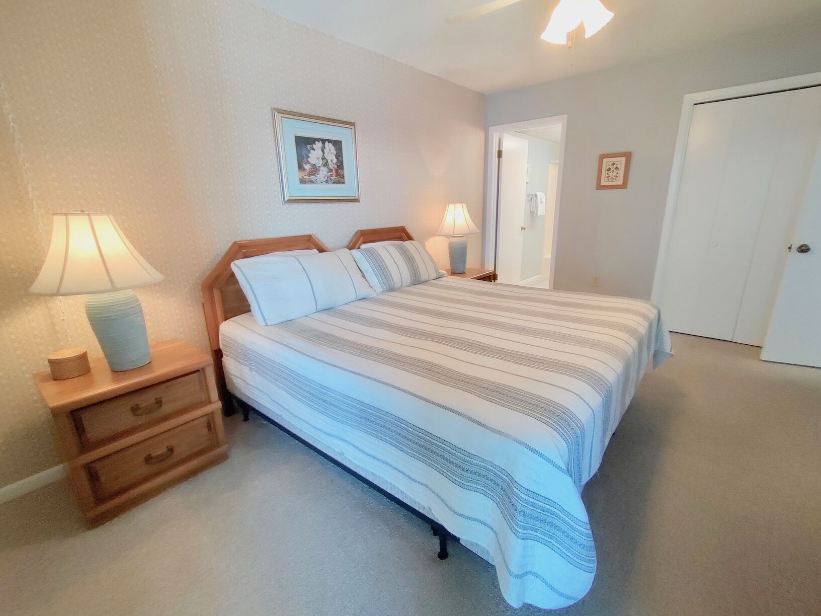 Een slaapkamer met een bed, twee nachtkastjes met lampen, een houten nachtkastje en een deur.