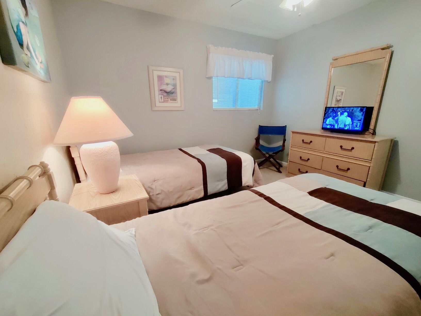 A hotel room with two beds, a nightstand with a lamp, a dresser, a chair, and a television on the dresser.