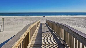Ein hölzerner Steg führt zu einem Strand mit blauem Himmel.