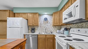 Una cocina con armarios de madera, un lavavajillas de acero inoxidable, un microondas, una estufa y un reloj en la pared.