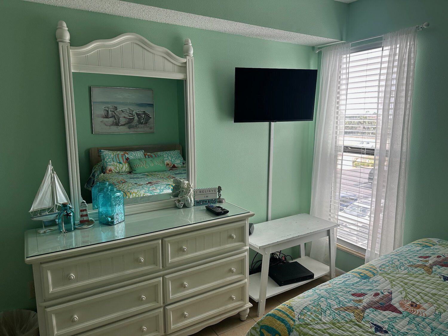 A bedroom with a bed, a dresser, a TV, and a window with blinds.