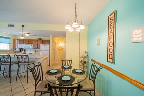 A dining area with a glass table, four chairs, and a hanging light fixture.