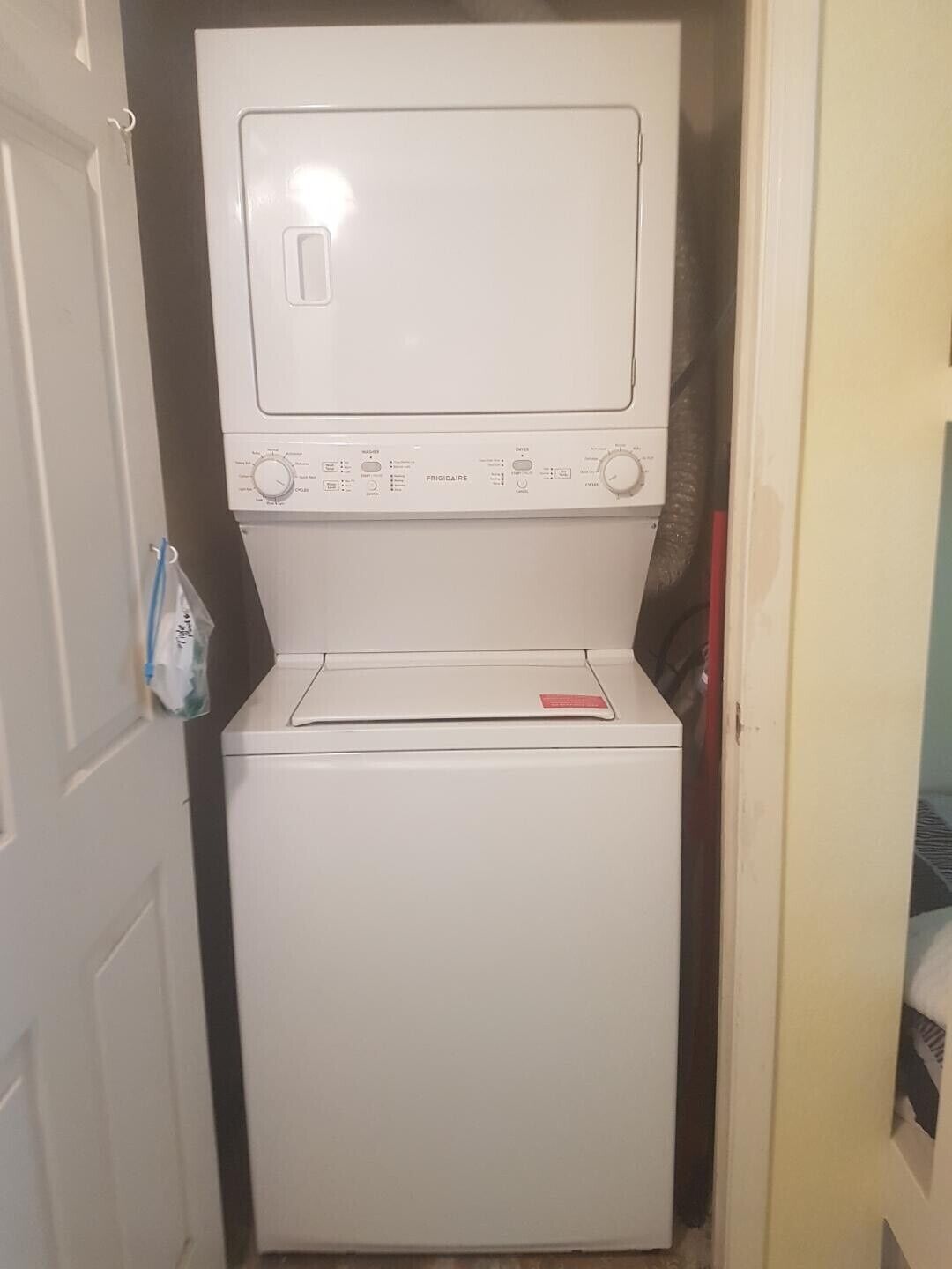 A compact, white front-loading washer and dryer unit with control panels and a small red tag on the door.