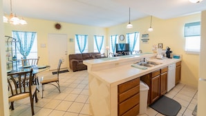 A kitchen with a central island, a dining area with a glass table, and a living area with a sofa.