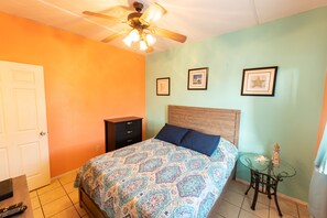 A bedroom with a bed, a ceiling fan, a nightstand, and a small table with a lamp.