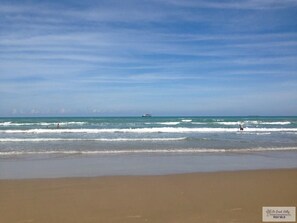 A beach with waves, a boat in the distance, and a clear sky.