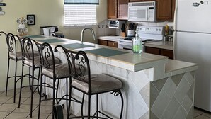 A kitchen with a central island, bar stools, wooden cabinets, a microwave, stove, and a refrigerator.