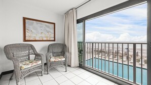 Un balcon avec deux fauteuils en osier, un tableau encadré et une vue sur une plage et une piscine.
