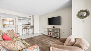 Un salon moderne avec un canapé, une table basse et un téléviseur fixé au mur, au-dessus d’une étagère en bois.