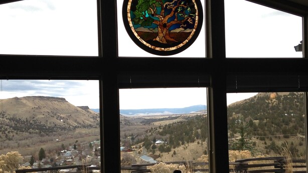 A view through a window with a stained glass depicting a tree, overlooking a valley with mountains, a town, and a wooden fence. - Vacation and Business Get-A-Way/Lay-Over (John Day)