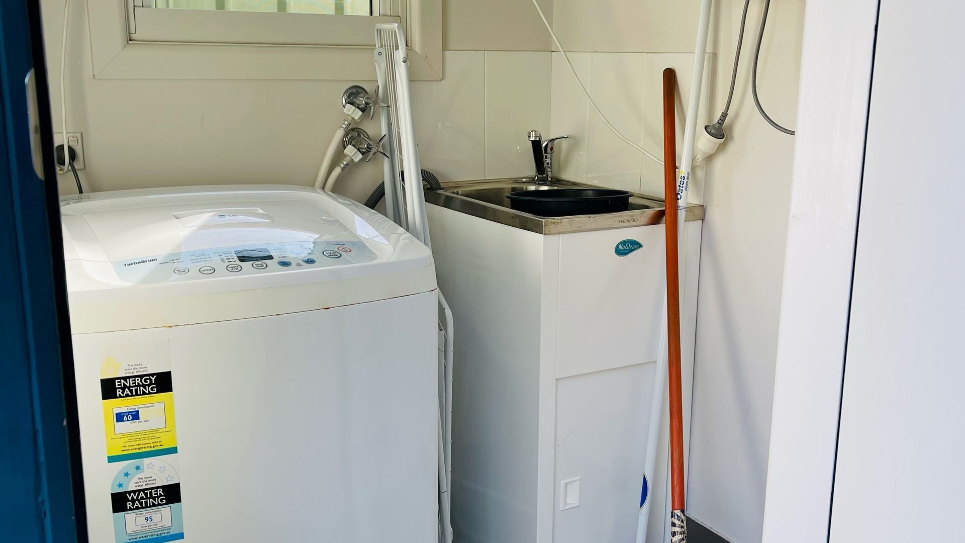 A compact laundry room with a front-loading washer and dryer, a small sink, and a mop leaning against the wall.