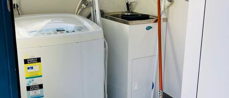 A compact laundry room with a front-loading washer and dryer, a small sink, and a mop leaning against the wall.
