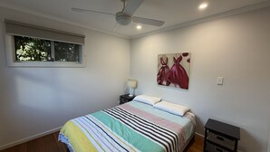 Une chambre à coucher avec un lit, un ventilateur de plafond, une fenêtre, une table de chevet, une lampe et un tableau.