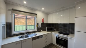 A modern kitchen with a window, stainless steel appliances, and black tiled backsplash. - The Osprey House - Quaint 2 bedroom cottage in the centre of town (SOUTH WEST ROCKS)